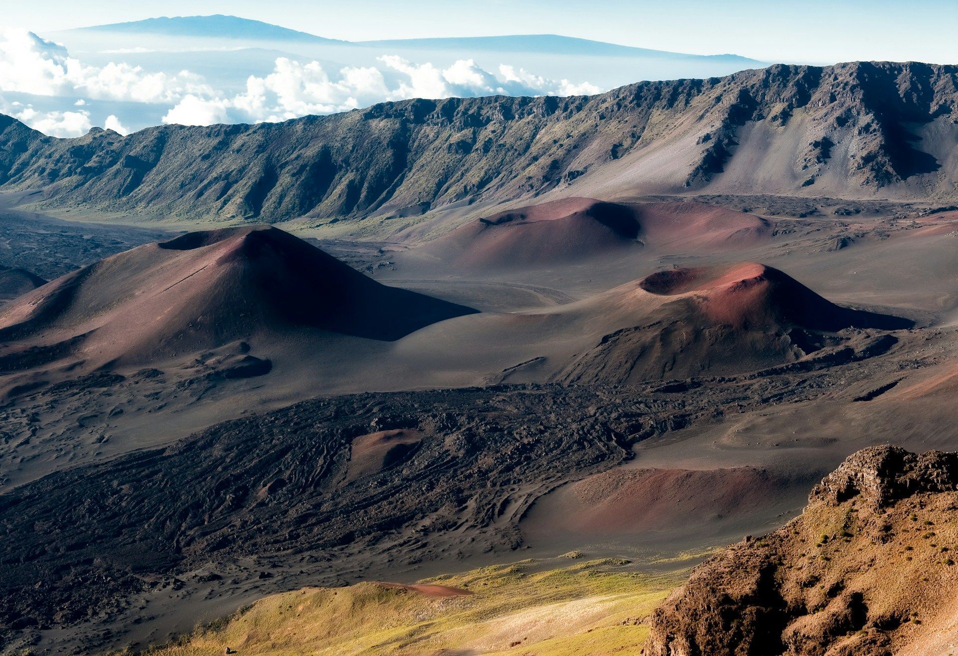 Un vasto paesaggio vulcanico caratterizzato da coni di scorie rossastre e colate di lava scure all'interno di una grande caldera sotto un cielo limpido.