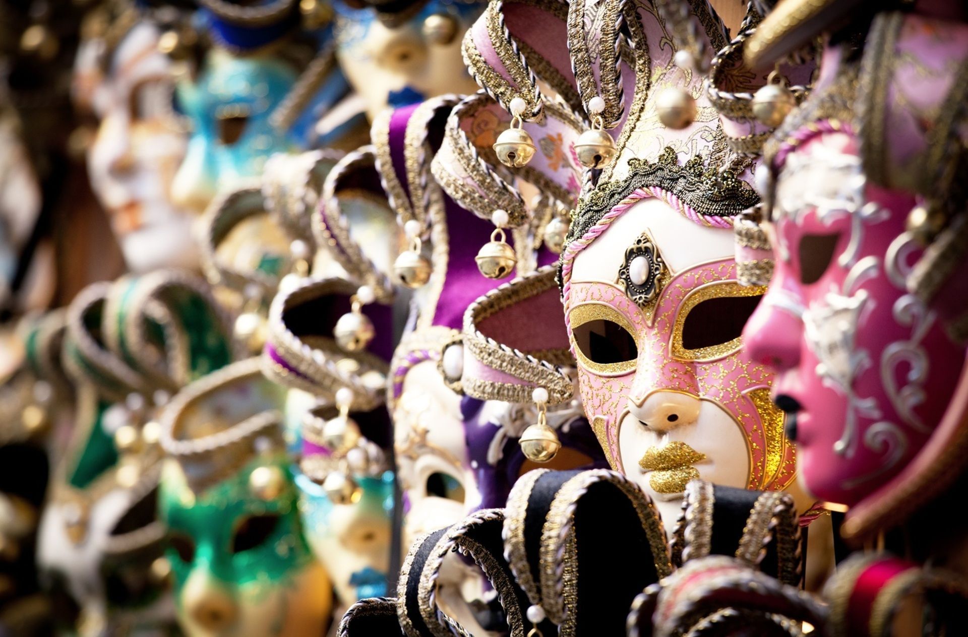 Une rangée de masques vénitiens colorés et ornés exposés, avec un masque rose et blanc mis en valeur.