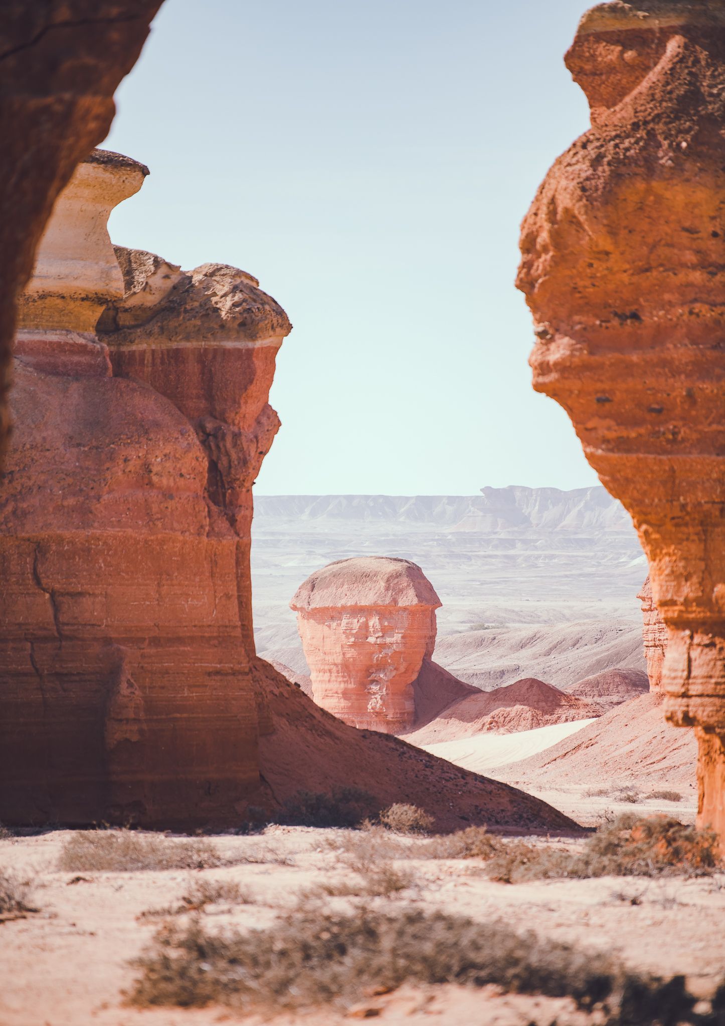 Una singolare formazione rocciosa rossa in un paesaggio desertico, ammirata attraverso una fessura nelle scogliere di arenaria.