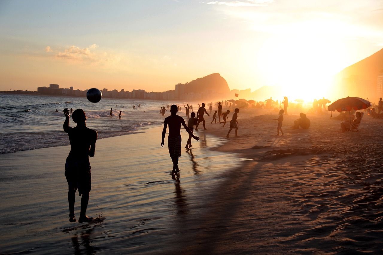 Silhouettes de personnes jouant au ballon sur une plage bondée au coucher du soleil sur l'océan et une ville lointaine