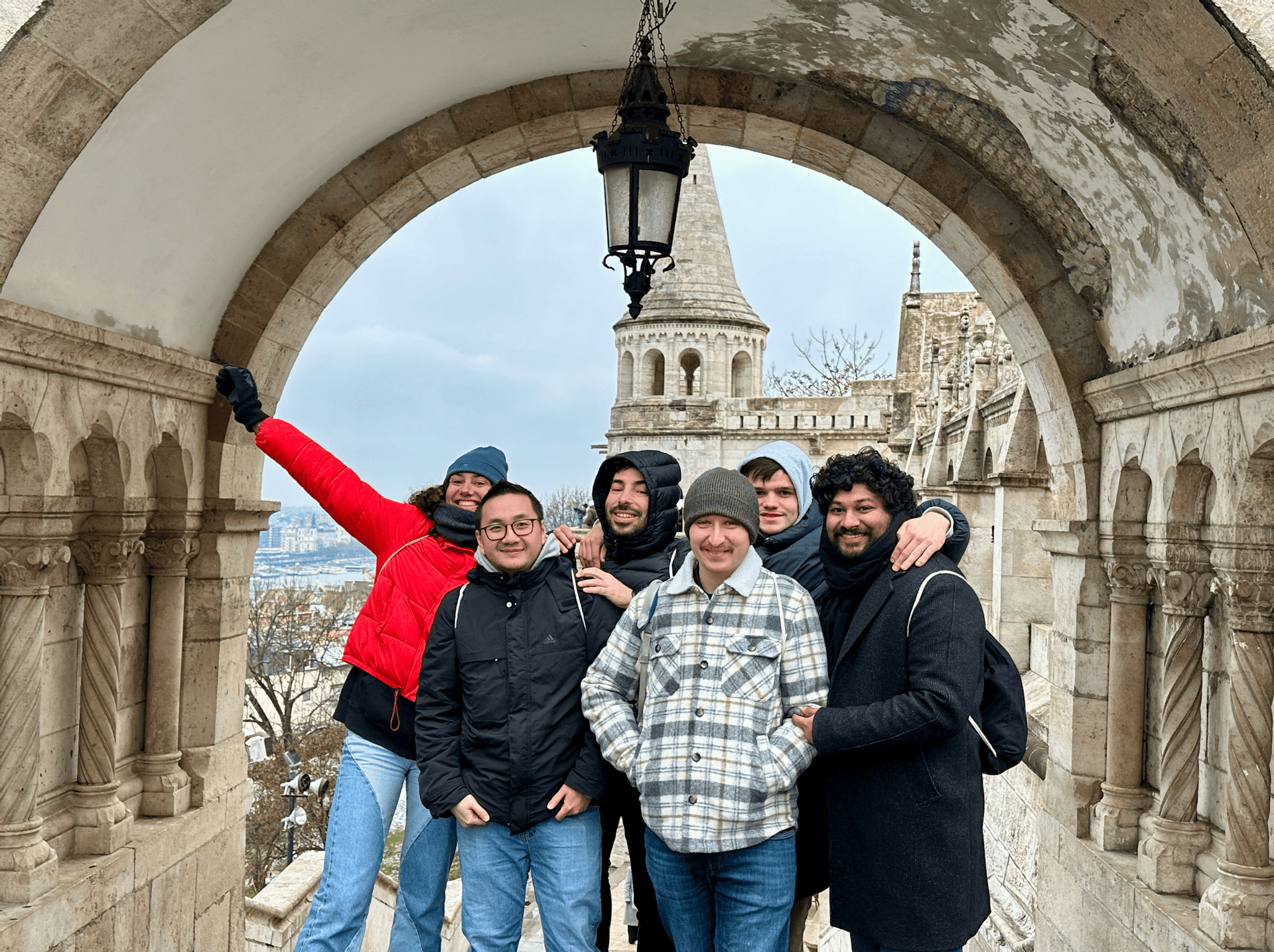 Un voyage de groupe WeRoad de six personnes posant pour une photo sous une arche en pierre, avec une tourelle de château visible en arrière-plan.