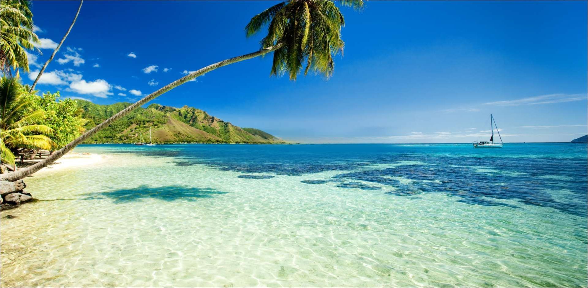 Rocky, tree-covered islands and a tall rock formation rise from turquoise water under a blue sky with white clouds.