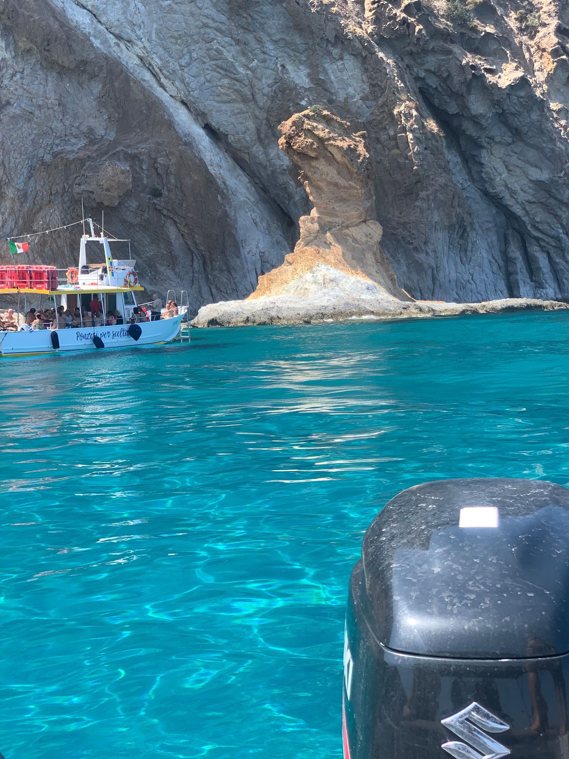 Un viaggio di gruppo WeRoad in barca navigando su acque cristalline e turchesi accanto a una scogliera rocciosa.
