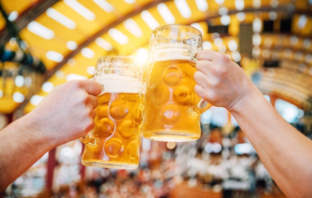 Due mani che brindano con grandi boccali di birra, su uno sfondo sfocato e ben illuminato.