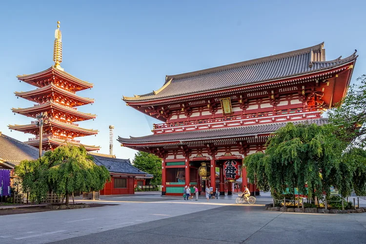 Una pagoda giapponese rossa a cinque piani e un grande portale del tempio si ergono in un cortile in una giornata di sole.