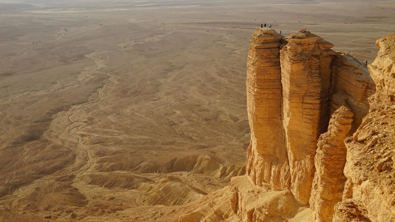 Un voyage de groupe WeRoad se tient sur une haute falaise surplombant un vaste canyon désertique sous un ciel voilé.