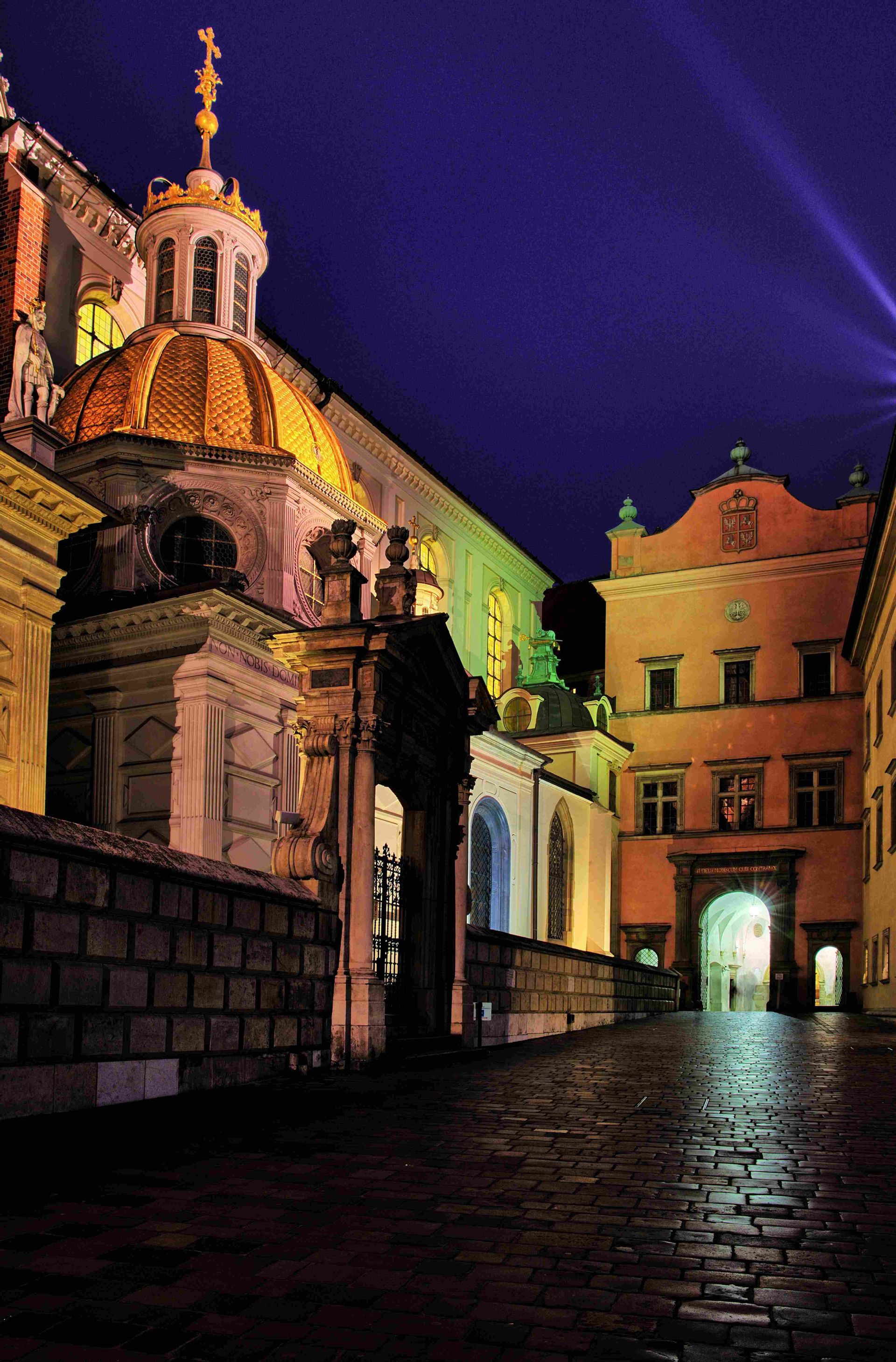 Una histórica calle empedrada de noche, con un edificio ornamentado que presenta una gran cúpula dorada iluminada contra un cielo oscuro.