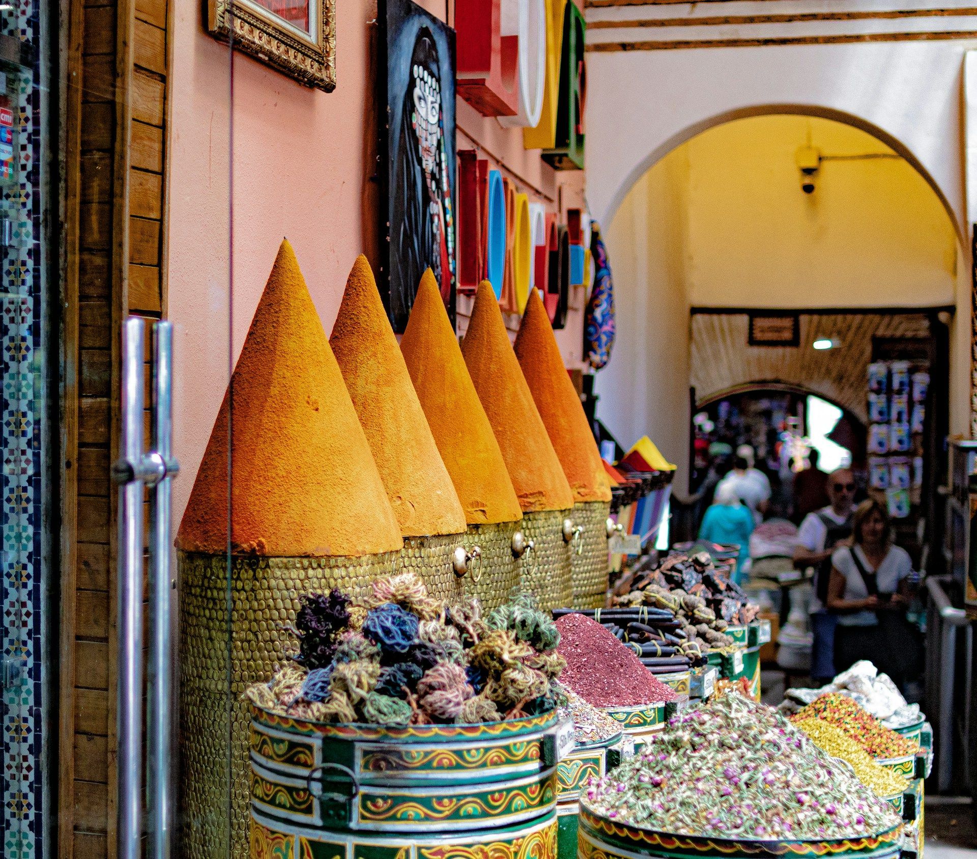 Tall cones of orange spices and colorful bins of dried herbs and flowers on display at an outdoor market stall.