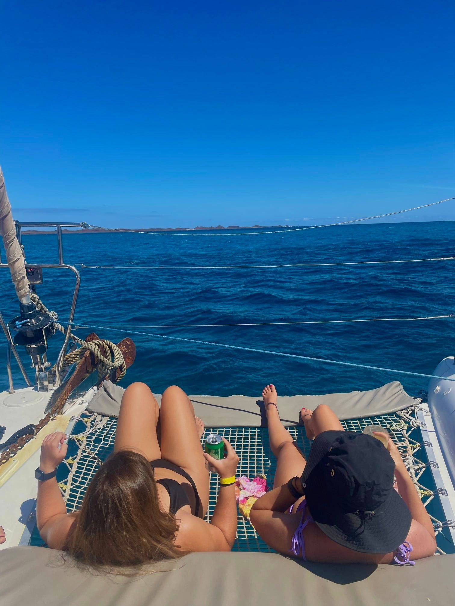 Dos mujeres de un viaje en grupo de WeRoad toman el sol en la red de un catamarán mientras navegan en el mar azul.