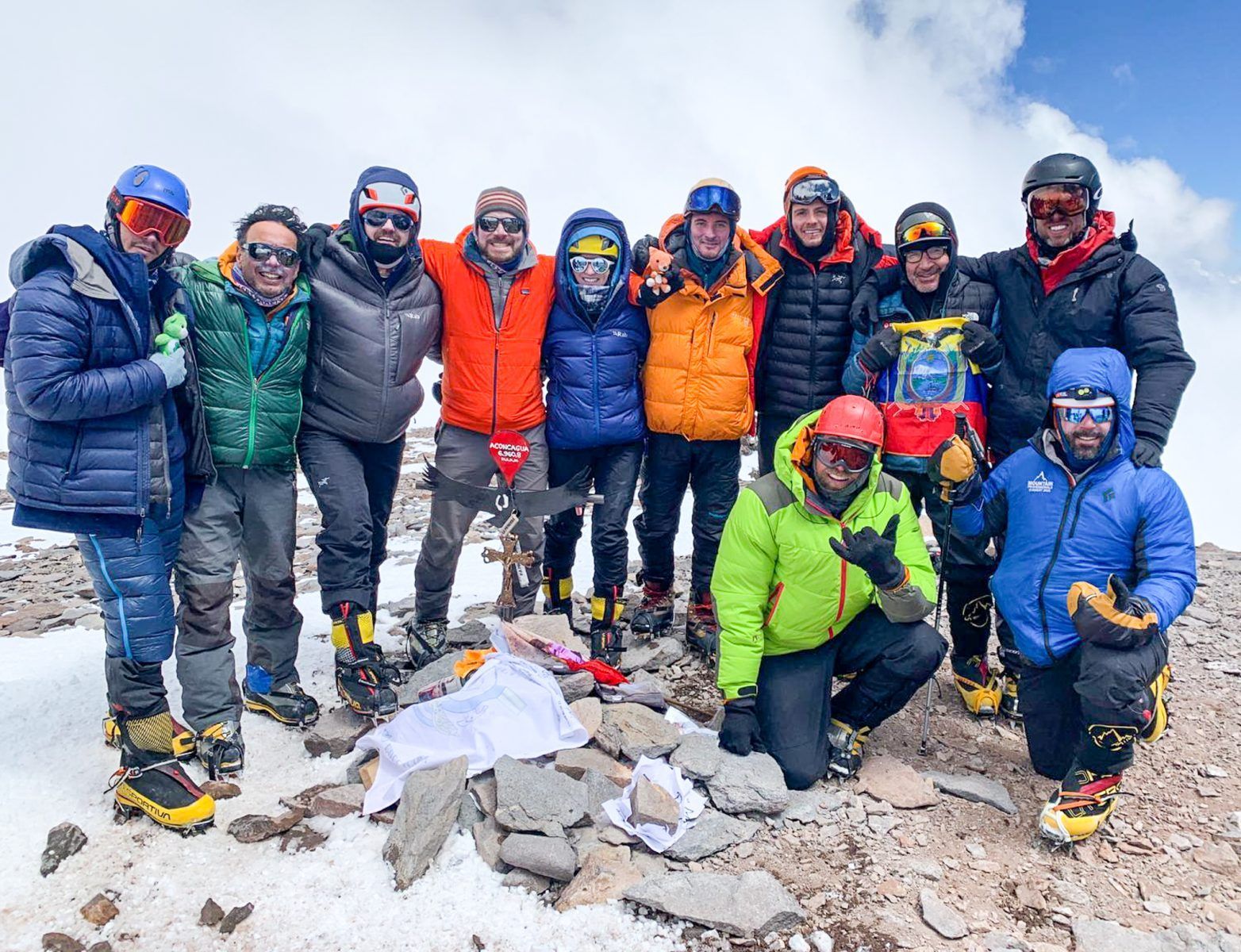 A WeRoad group trip of people in mountaineering gear posing for a photo on a snowy, rocky mountain summit.