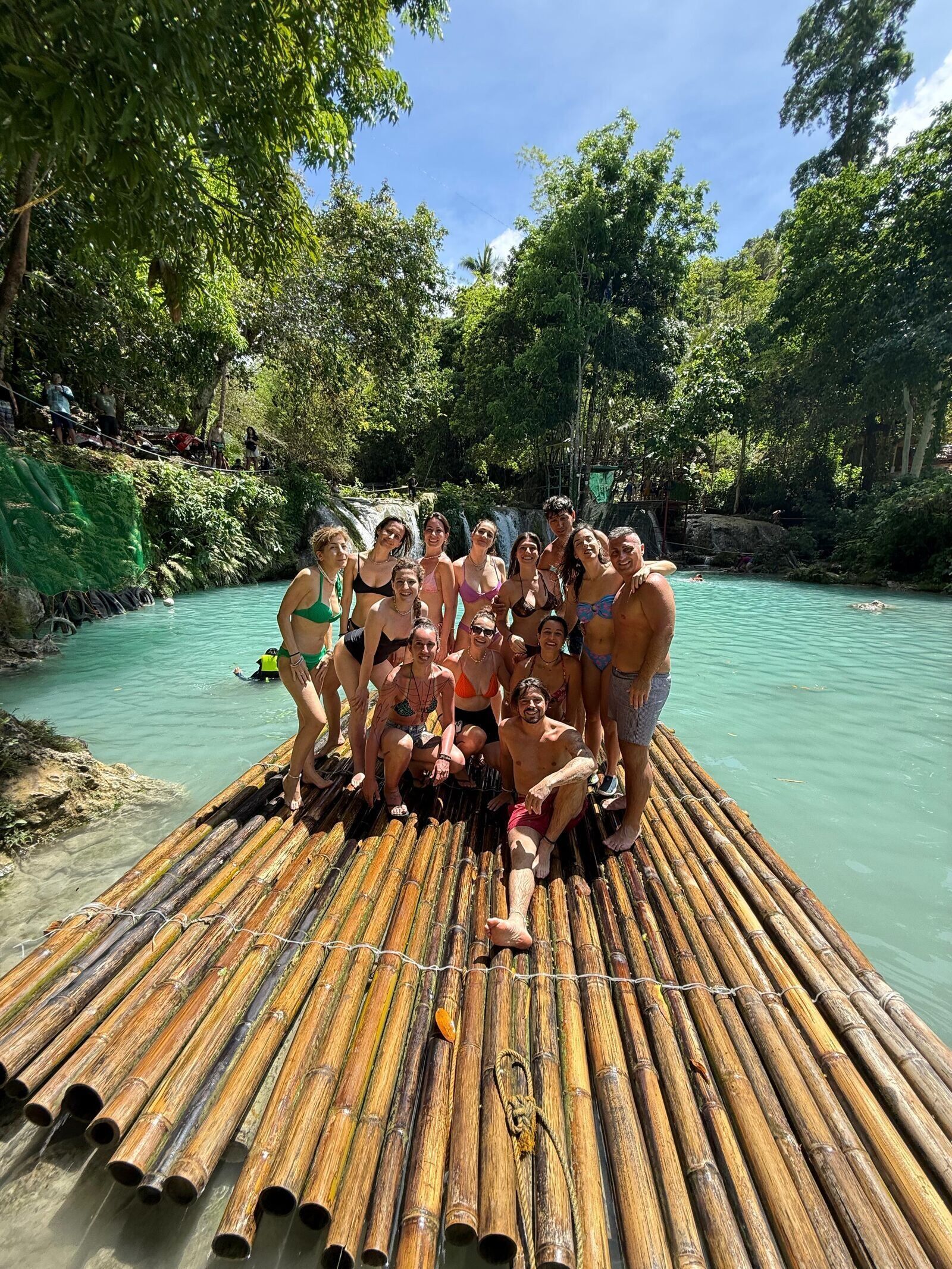 Un viaggio di gruppo WeRoad con persone in costume da bagno che posano insieme su una grande zattera di bambù, su un fiume turchese in una foresta lussureggiante.