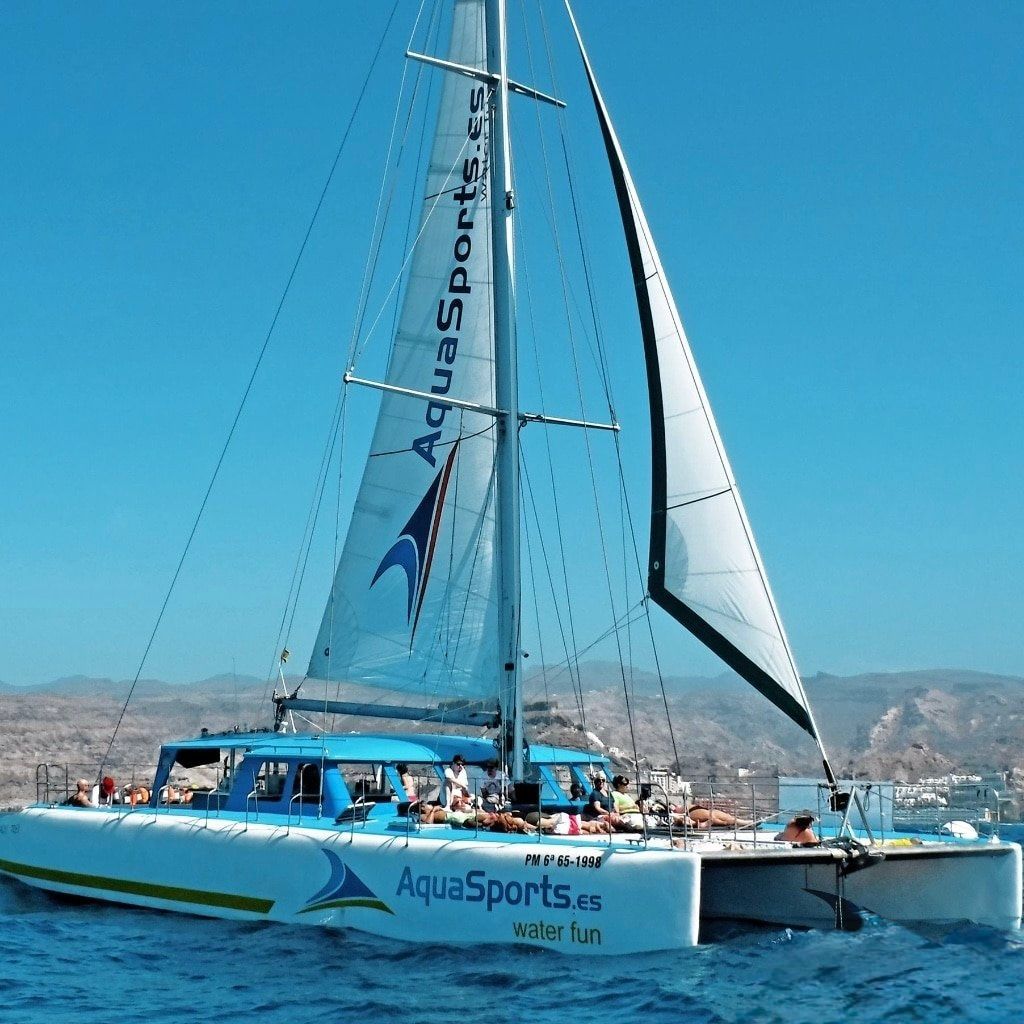A WeRoad group trip relaxing on the deck of a large catamaran sailing across the ocean on a sunny day.
