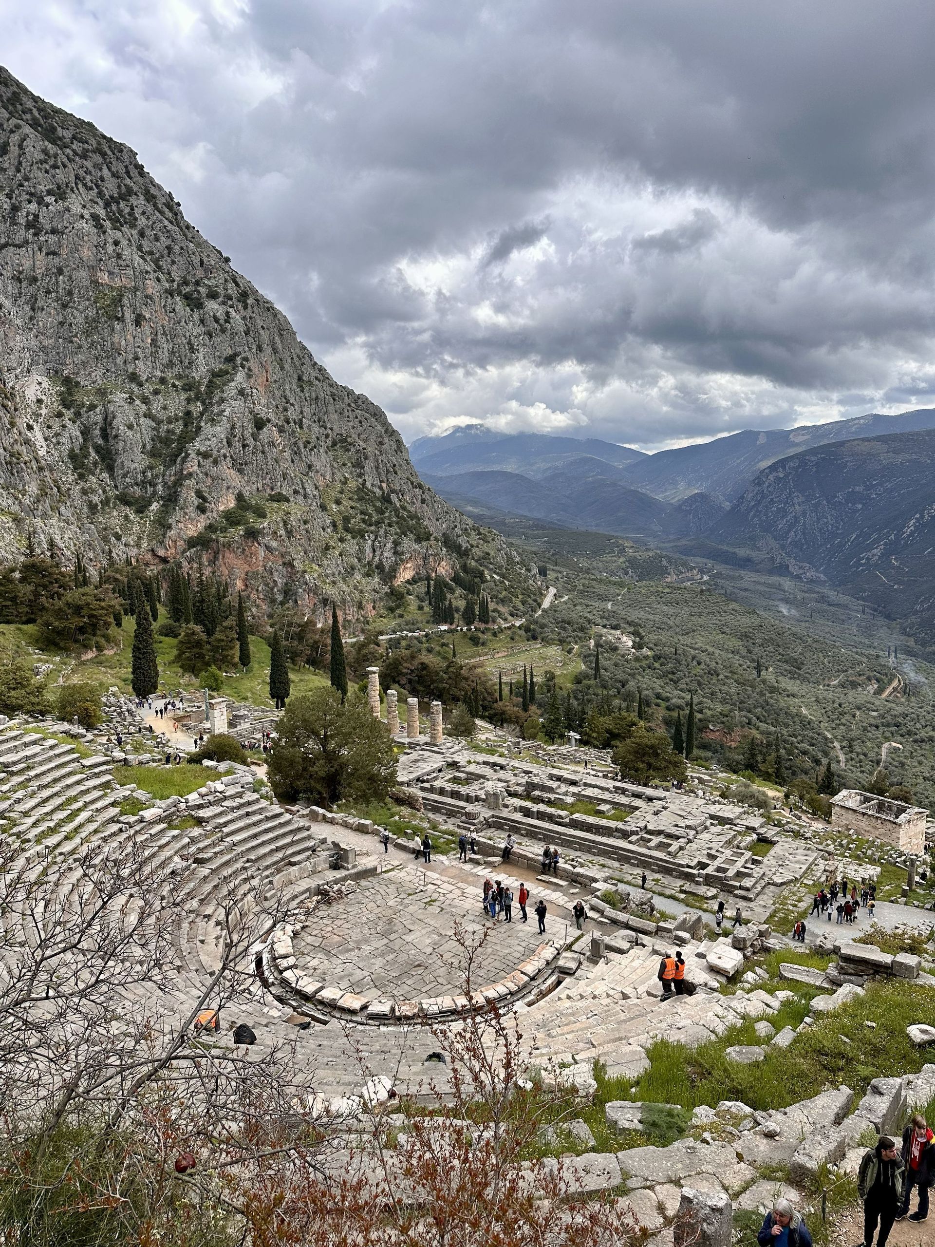 Veduta dall'alto di un antico anfiteatro in pietra e rovine incastonate nel fianco di una montagna, con un gruppo WeRoad che esplora il sito.
