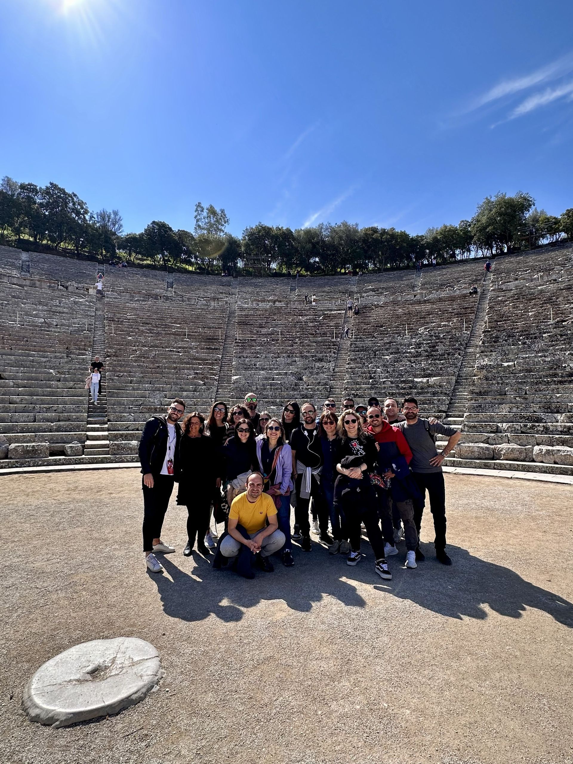 Un gruppo WeRoad posa per una foto al centro di un grande anfiteatro in pietra sotto un cielo azzurro.