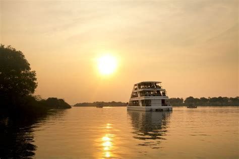 Una barca a più ponti con a bordo un viaggio di gruppo WeRoad naviga su un fiume calmo durante un tramonto dorato.