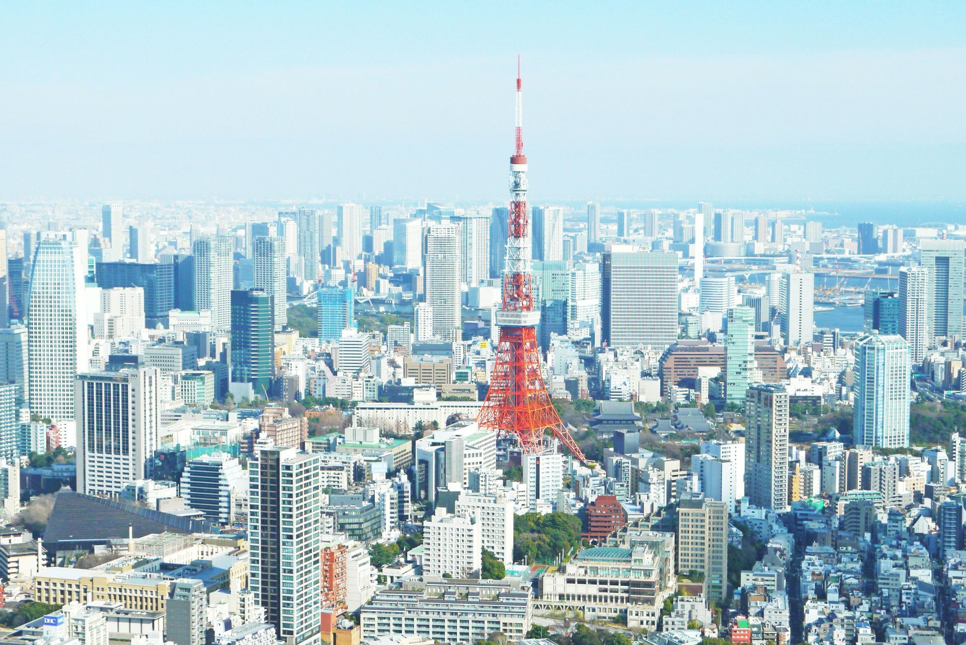 Vue aérienne d'une tour en treillis rouge et blanc au centre d'un paysage urbain dense avec de nombreux gratte-ciel.