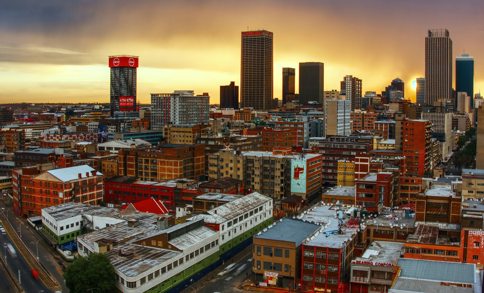 A sprawling cityscape with a mix of low-rise buildings and tall skyscrapers under a golden sunset sky.