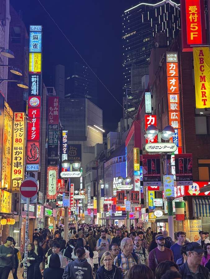 Un viaggio di gruppo WeRoad percorre una vivace strada cittadina di notte, illuminata da alti edifici e colorate insegne al neon giapponesi.