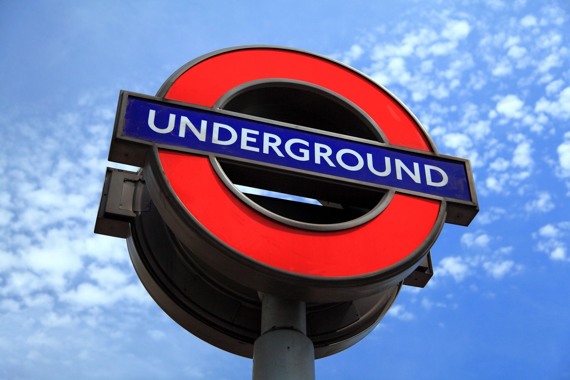 El letrero circular rojo del metro de Londres visto desde abajo contra un cielo azul con nubes blancas.