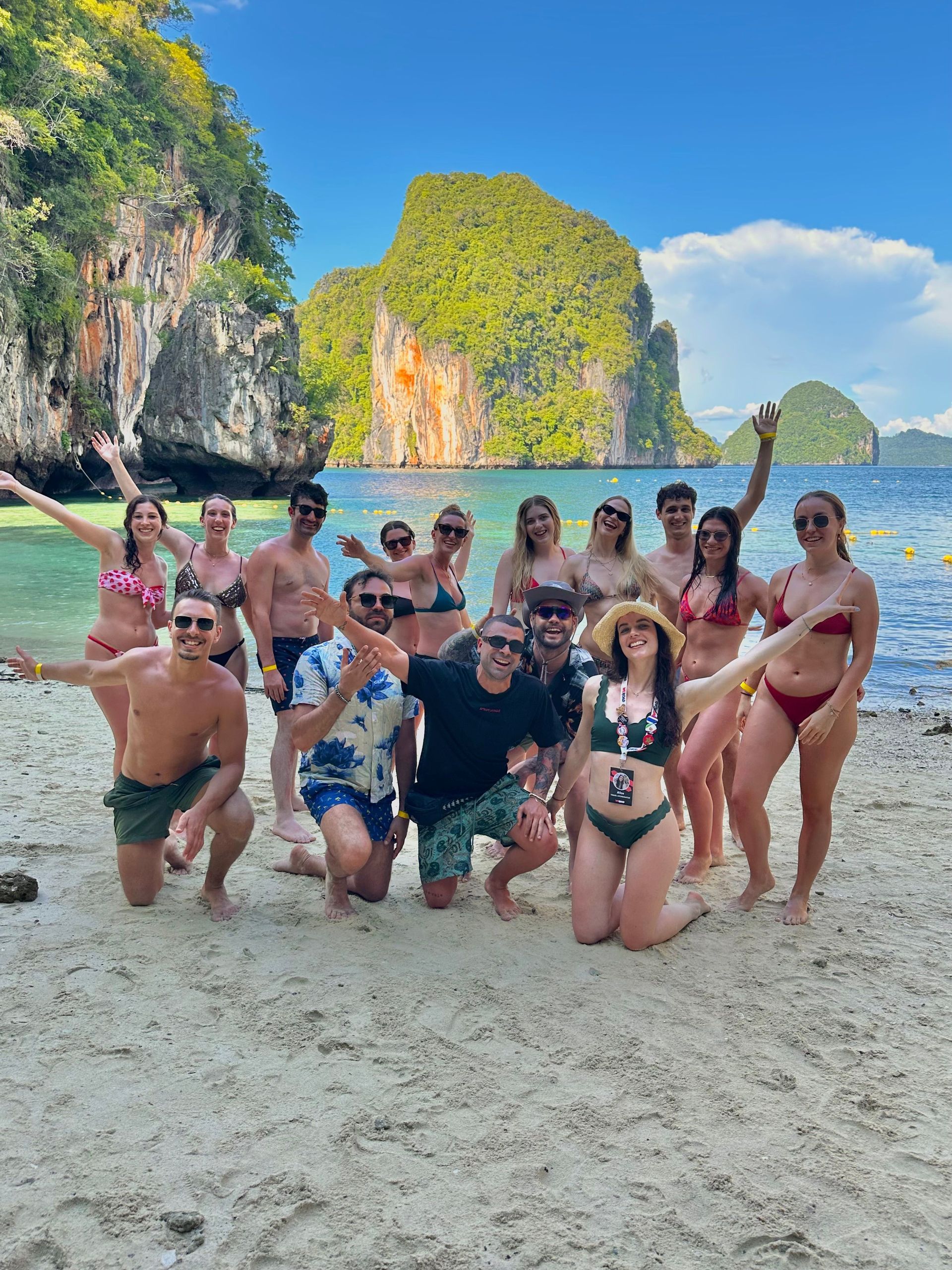 Un viaje en grupo de WeRoad en traje de baño posando para una foto en una playa de arena con islas rocosas verdes al fondo.
