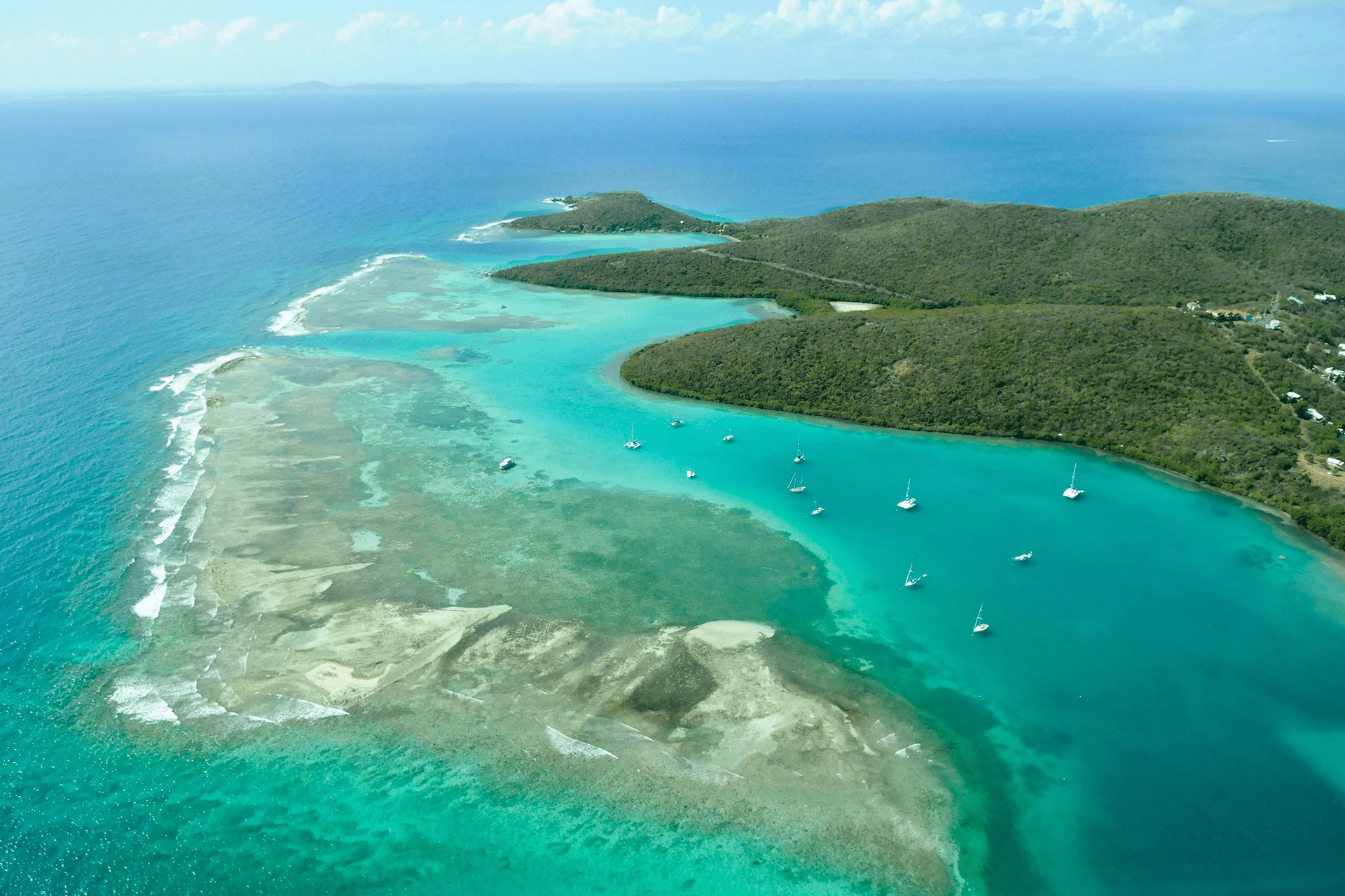 Una vista aerea di una penisola insulare verde e tropicale con barche a vela ancorate nelle calme acque turchesi di una baia.