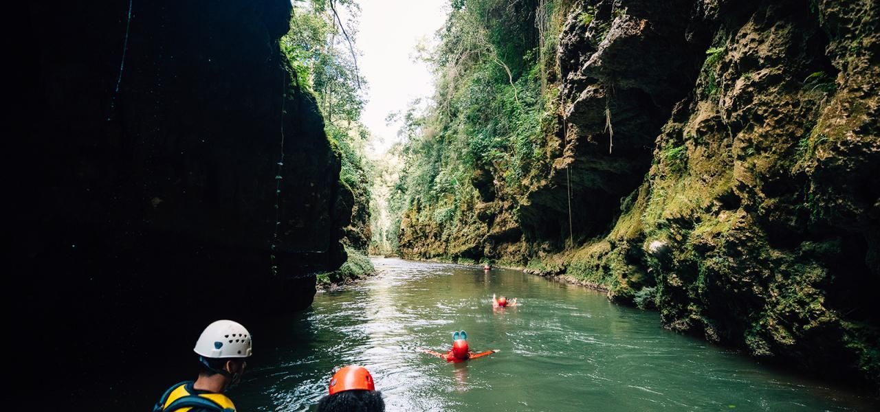 Un viaggio di gruppo WeRoad, con caschi e giubbotti di salvataggio, scende lungo un fiume attraverso uno stretto e lussureggiante canyon verde.