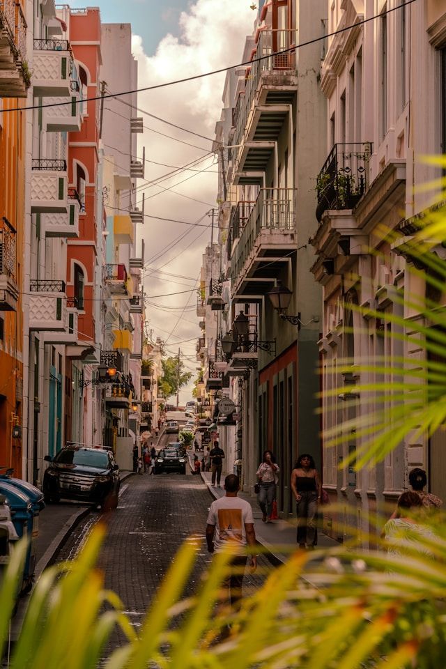 Una veduta su una stretta strada acciottolata, con persone che passeggiano tra colorati edifici a più piani dotati di balconi.