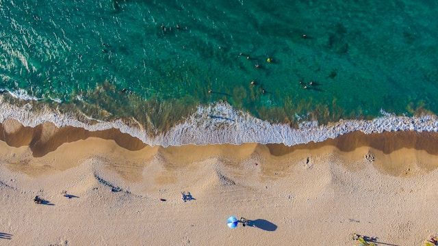 Vista aerea di una spiaggia dove le persone nuotano nel mare turchese e si rilassano sulla sabbia.