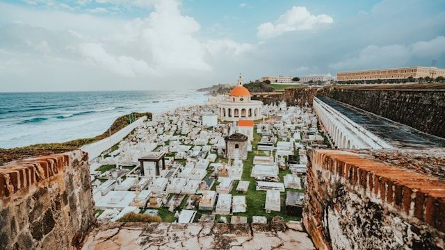 Veduta dall'alto di un cimitero costiero con lapidi bianche e una cappella dalla cupola arancione, affacciato sull'oceano.