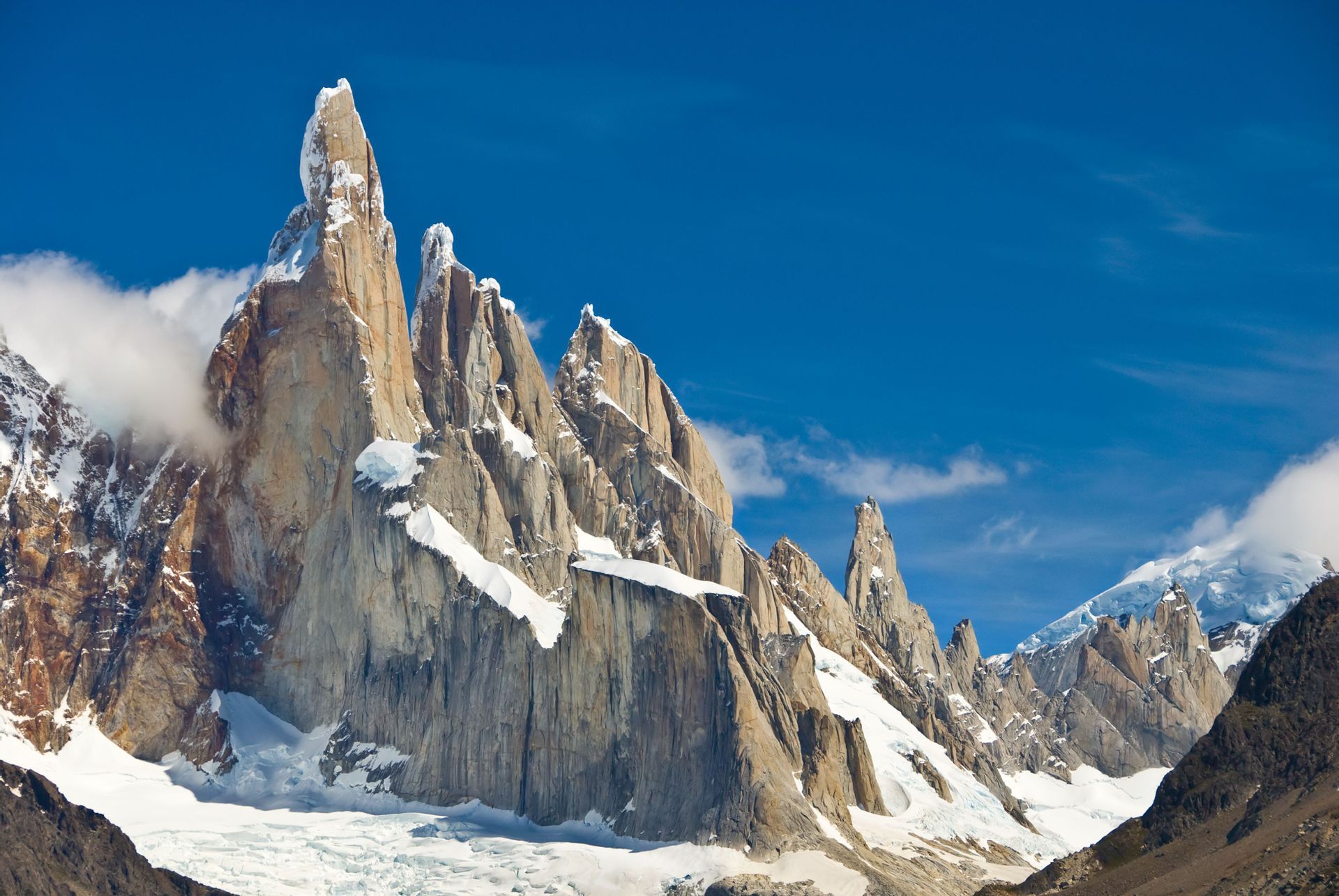 Zerklüftete Granit-Bergspitzen mit Schneefeldern und einem Gletscher am Fuße unter klarem blauem Himmel.