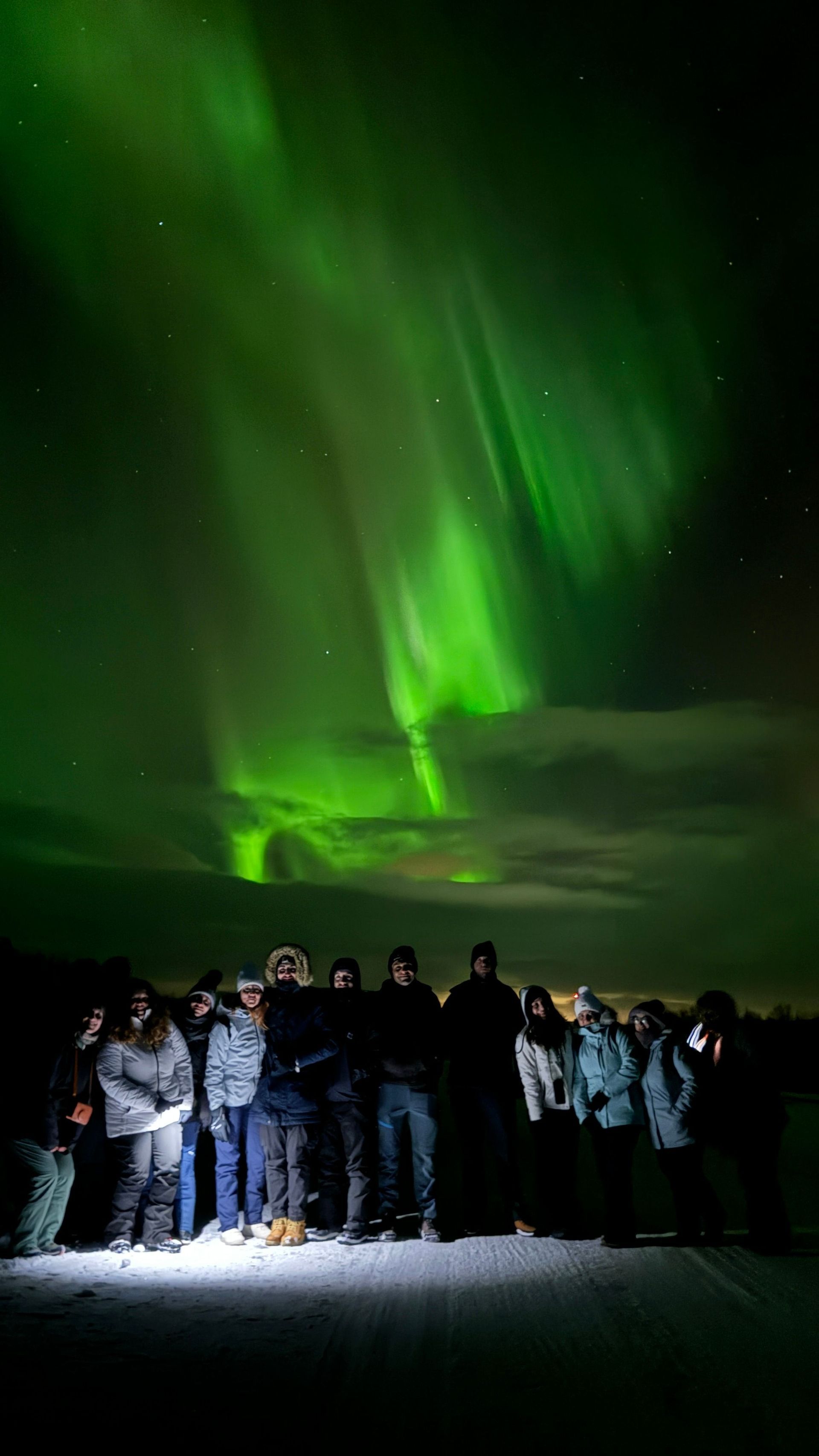 Un gruppo WeRoad in posa di notte su un paesaggio innevato sotto l'aurora boreale verde.
