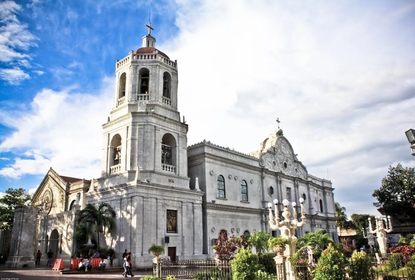 Una grande cattedrale in pietra bianca con un campanile ornato si erge sotto un cielo blu con nuvole bianche.