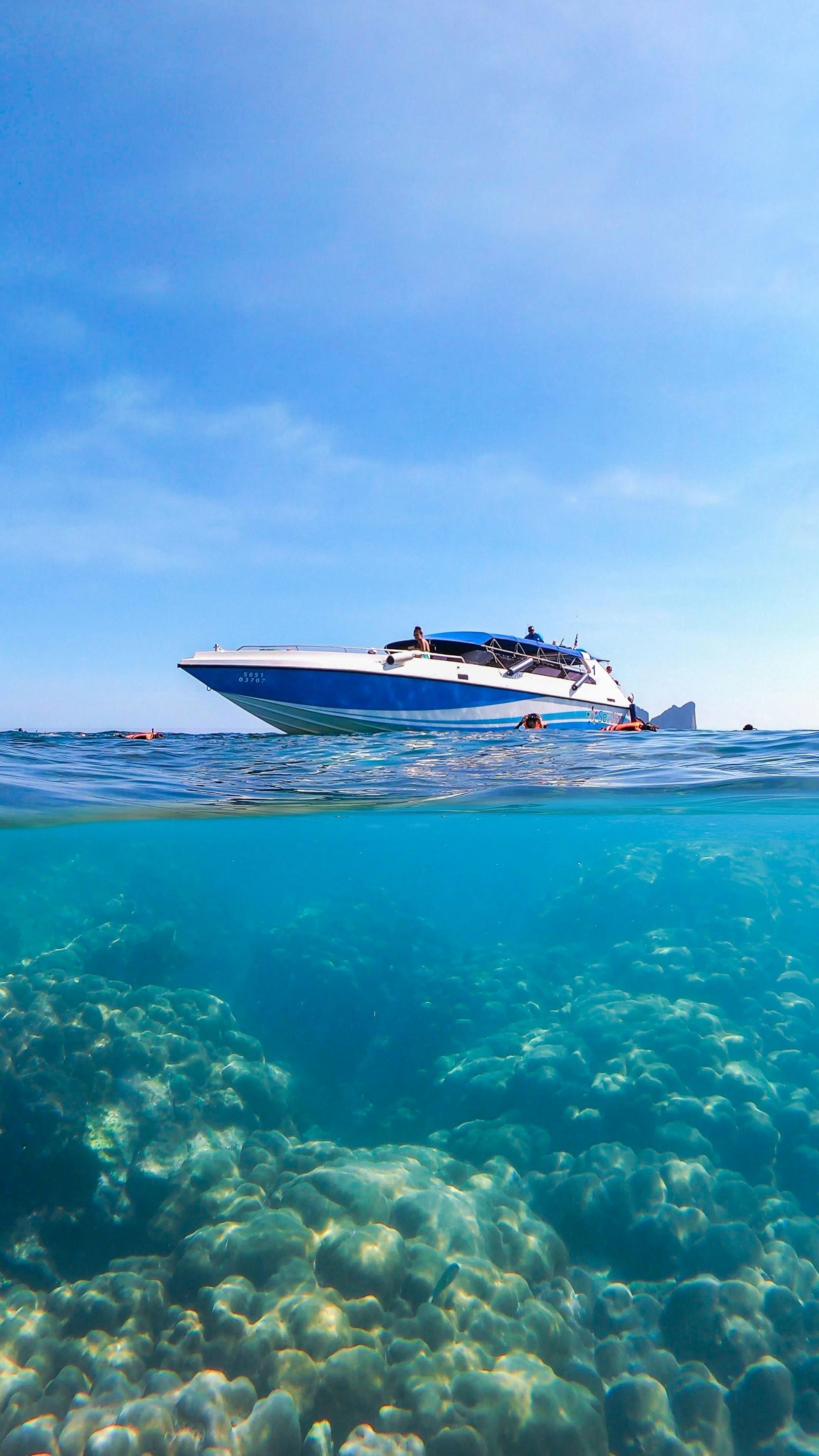 Una vista split-shot di un motoscafo in superficie e di un gruppo WeRoad che fa snorkeling su una barriera corallina.