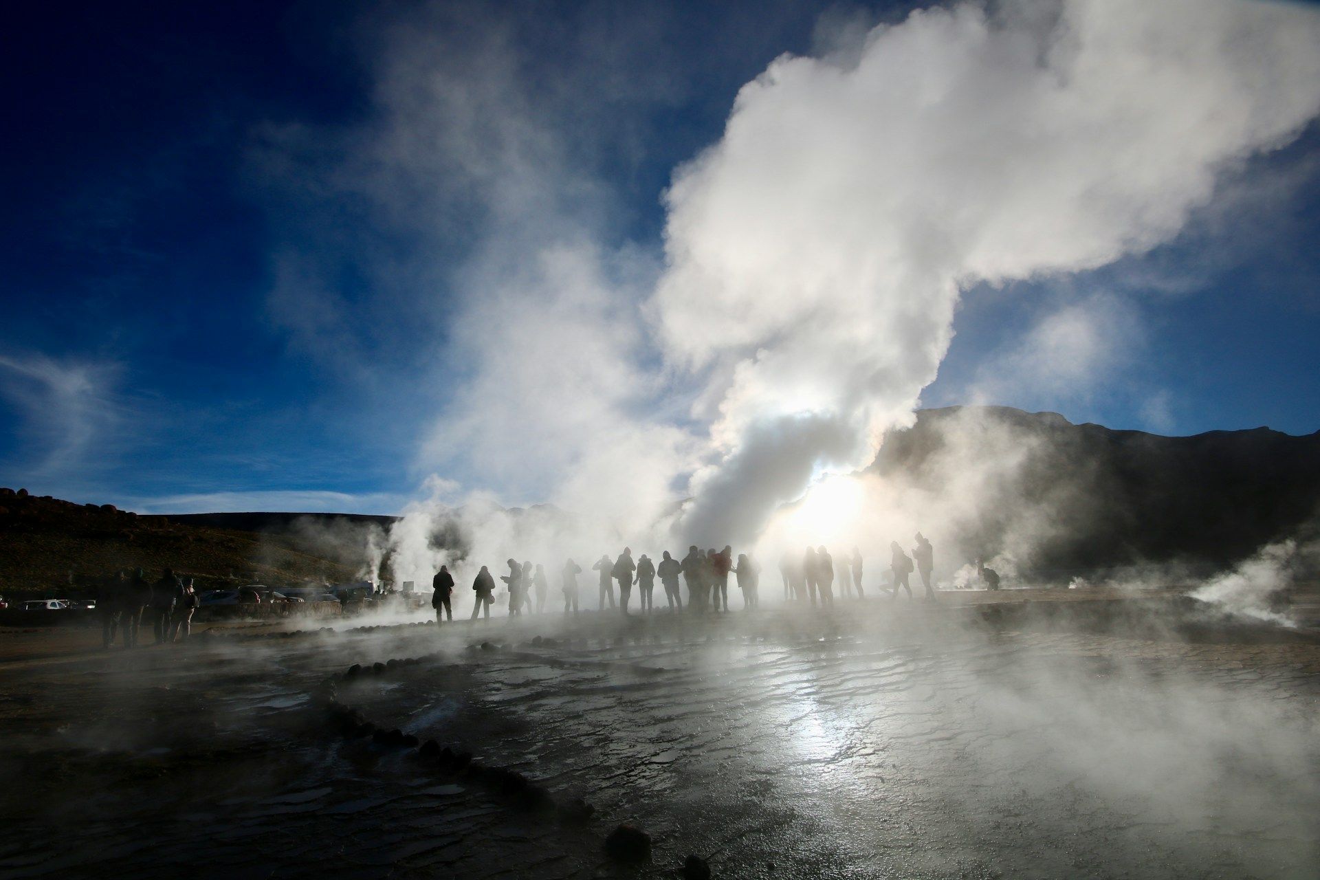 Sagome di un gruppo WeRoad tra geyser in eruzione, con vapore che si innalza contro un sole splendente e un cielo blu.