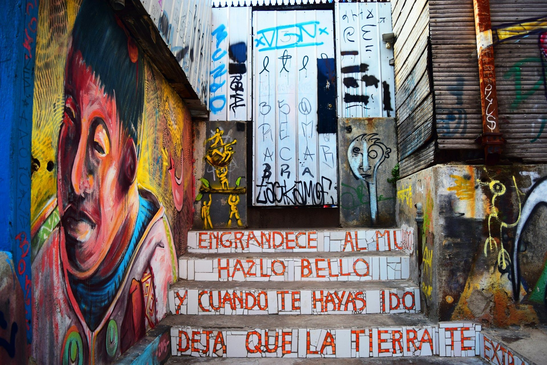 Una stretta scalinata esterna coperta di graffiti colorati, con un grande murale sulla parete sinistra e scritte a mosaico sui gradini.