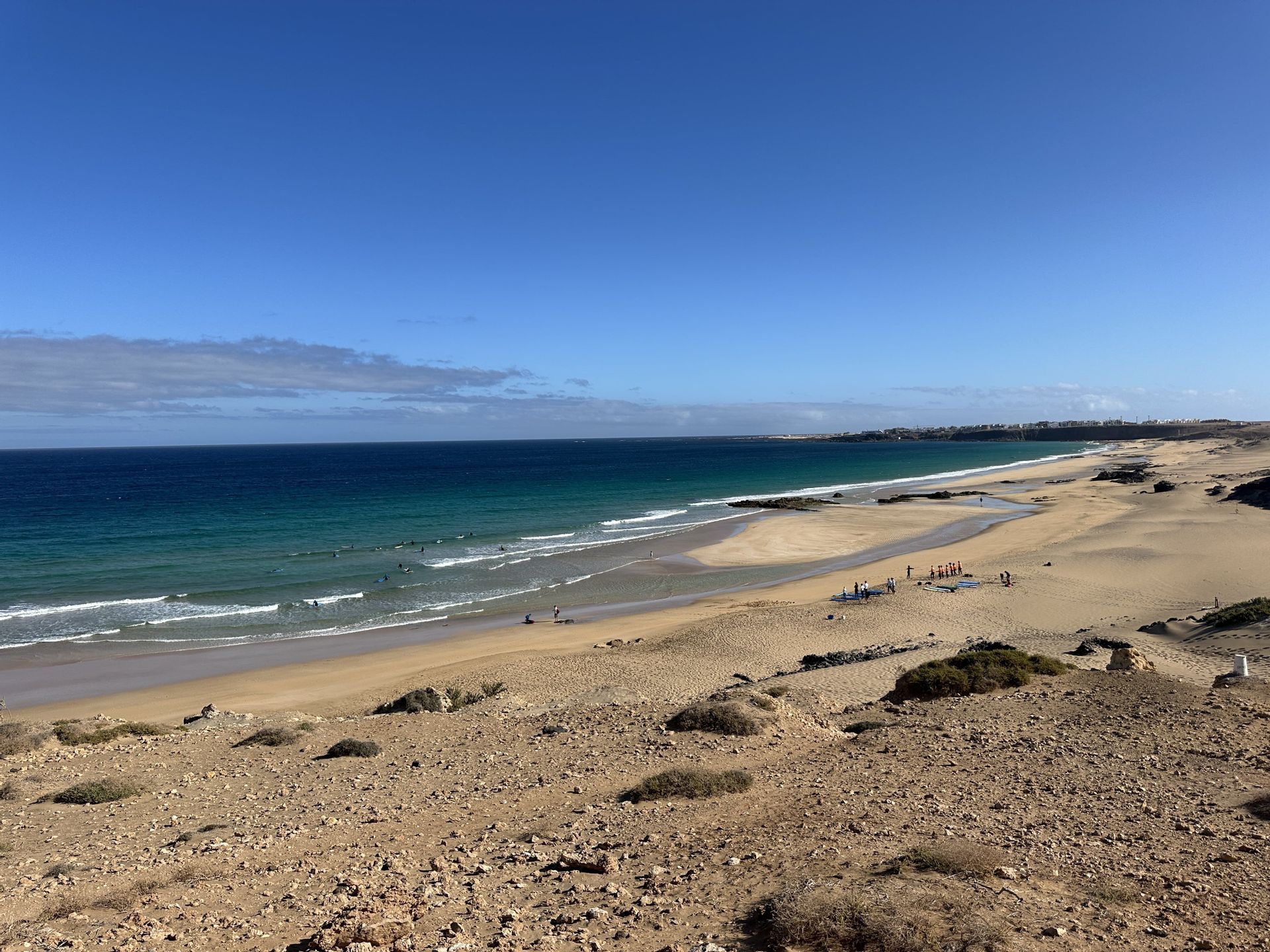 Vue panoramique d'un littoral sablonneux avec un groupe WeRoad prenant des cours de surf sur la plage et dans l'océan turquoise.