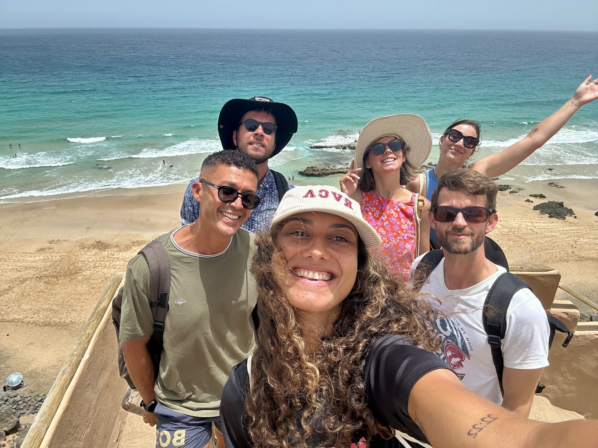 Un groupe WeRoad prend un selfie sur un point de vue surplombant une plage de sable et un océan turquoise.