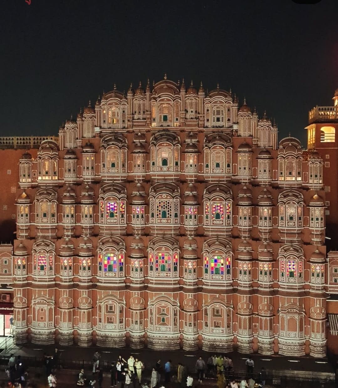 La facciata sontuosa di un palazzo in arenaria con centinaia di piccole finestre illuminate da luci colorate contro il cielo notturno.