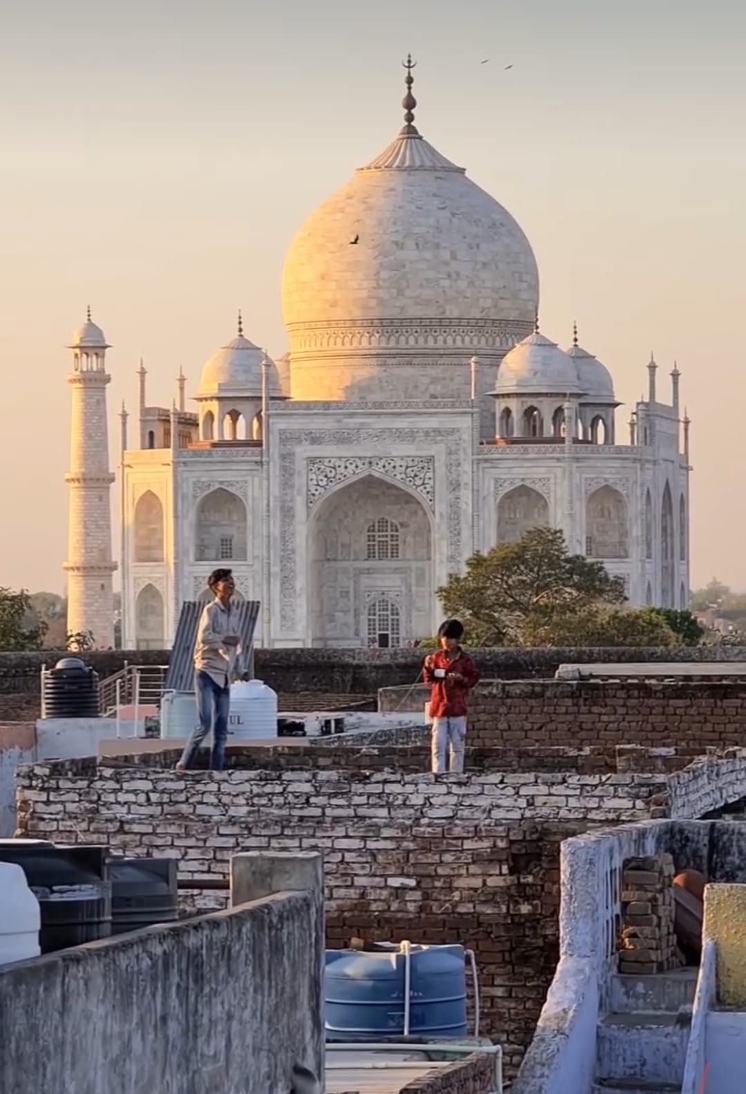 Due ragazzi su un tetto fanno volare aquiloni con il Taj Mahal sullo sfondo al tramonto.