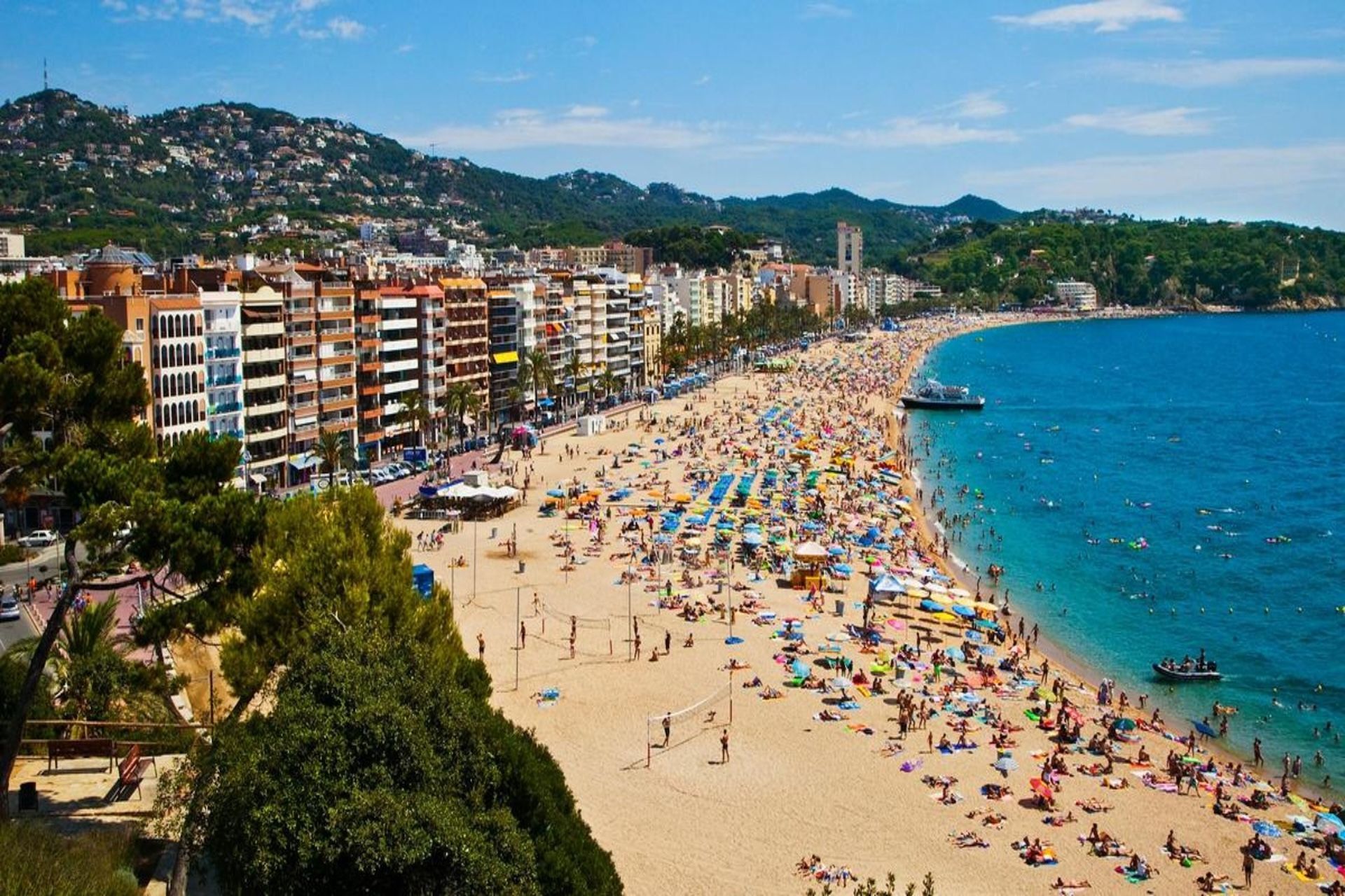Una vista aerea di una spiaggia sabbiosa affollata accanto a una città costiera, con persone che prendono il sole e nuotano nell'oceano blu.