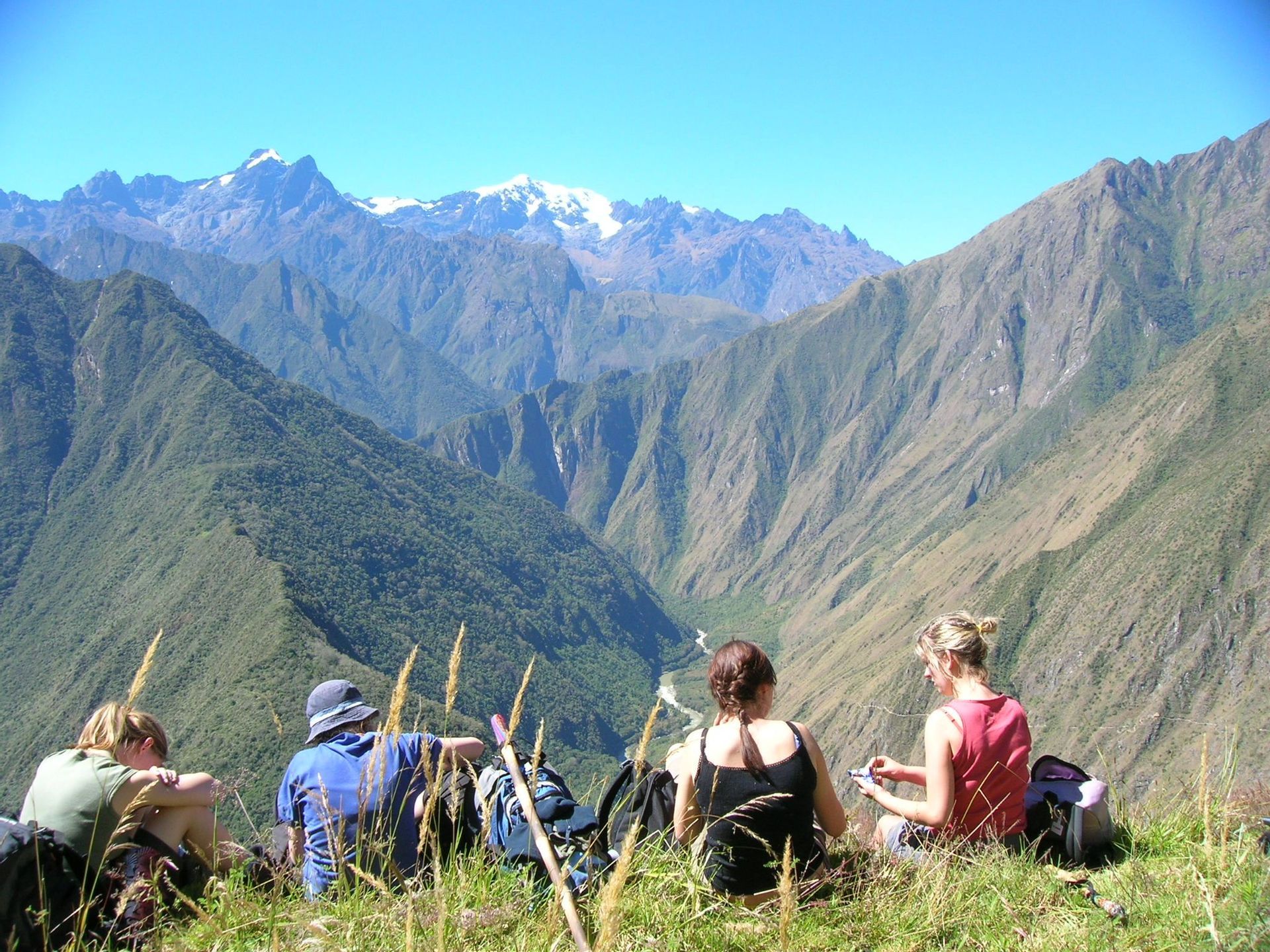 A WeRoad group trip sits on a grassy slope, looking out at a valley and distant snow-capped mountains.