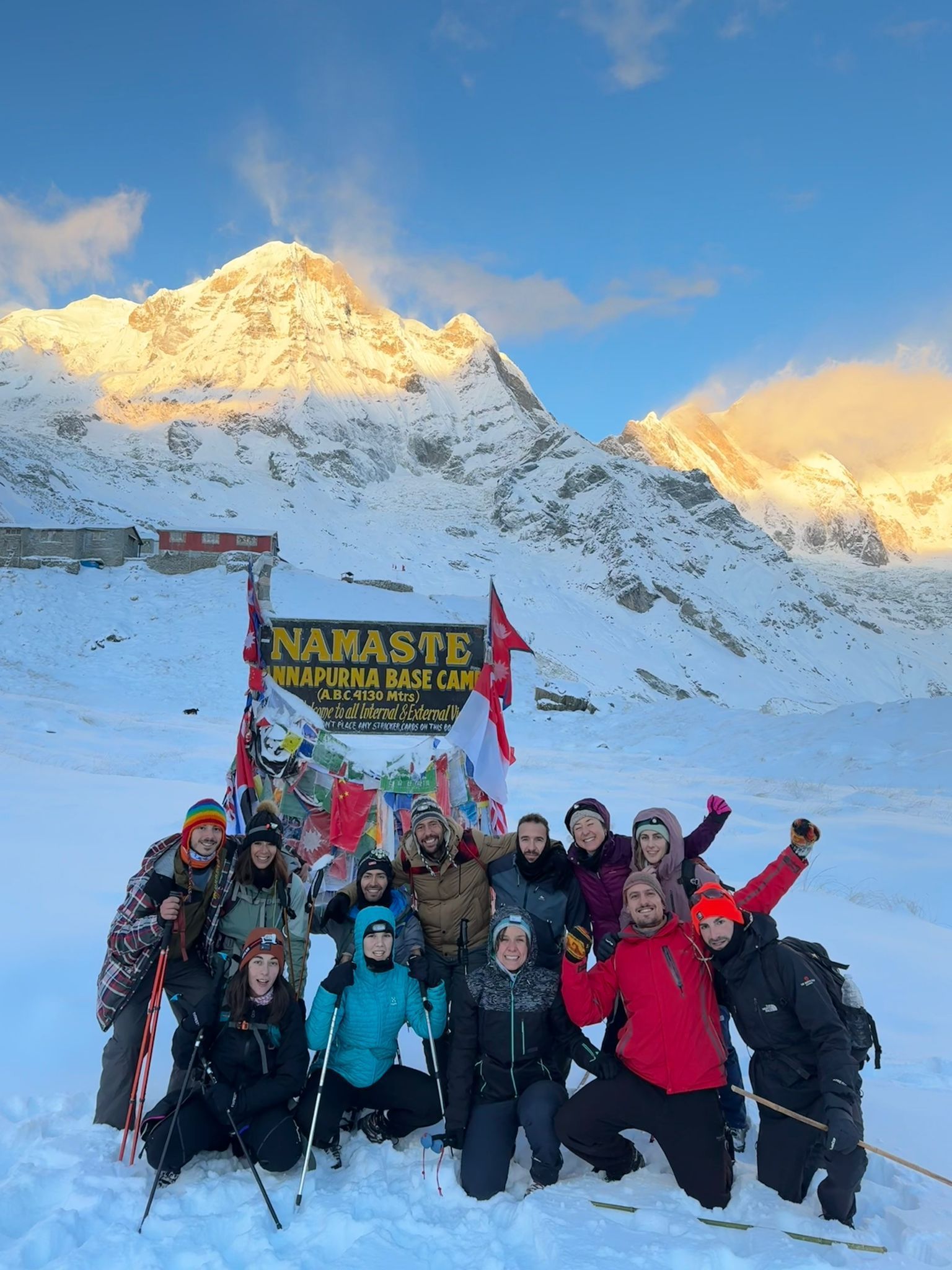 Un groupe WeRoad pose pour une photo devant le panneau du camp de base de l'Annapurna, avec des montagnes enneigées en arrière-plan.