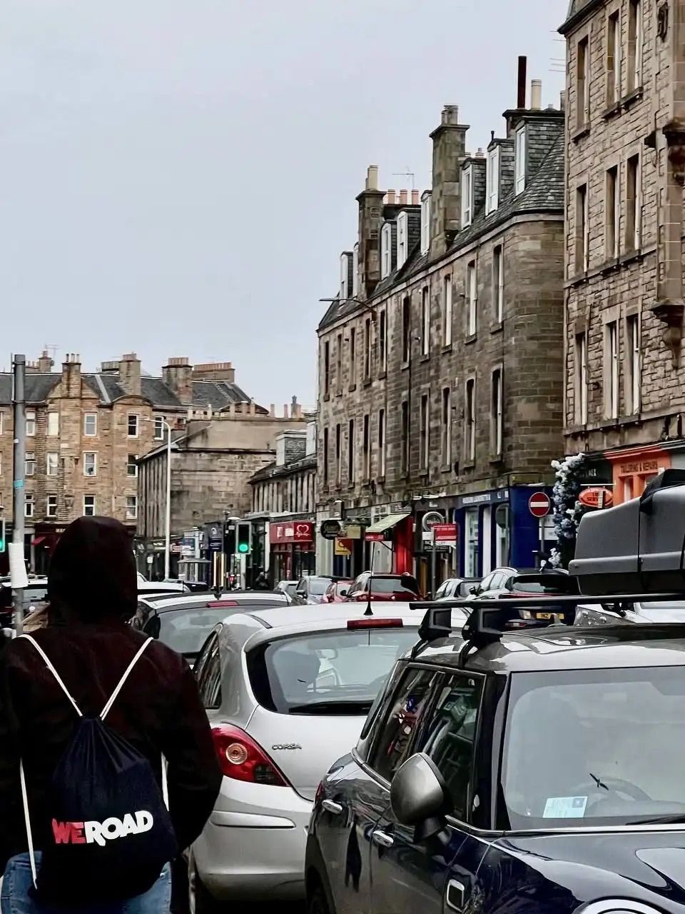 A person wearing a WeRoad backpack stands on a busy city street with traffic and stone buildings.