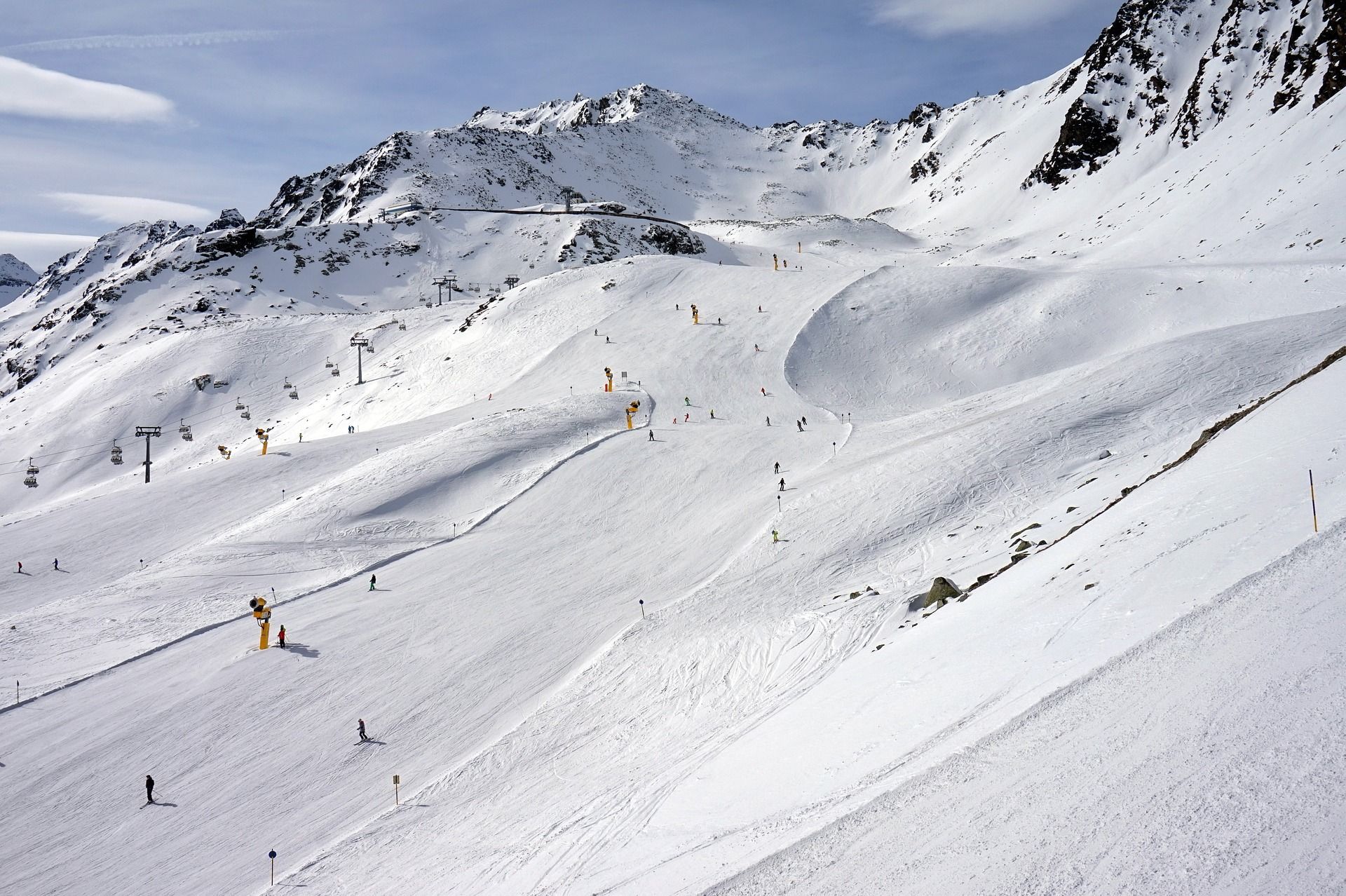 Une vue large d'une piste de ski animée avec de nombreuses personnes dévalant la pente, entourée de montagnes enneigées et de remontées mécaniques.