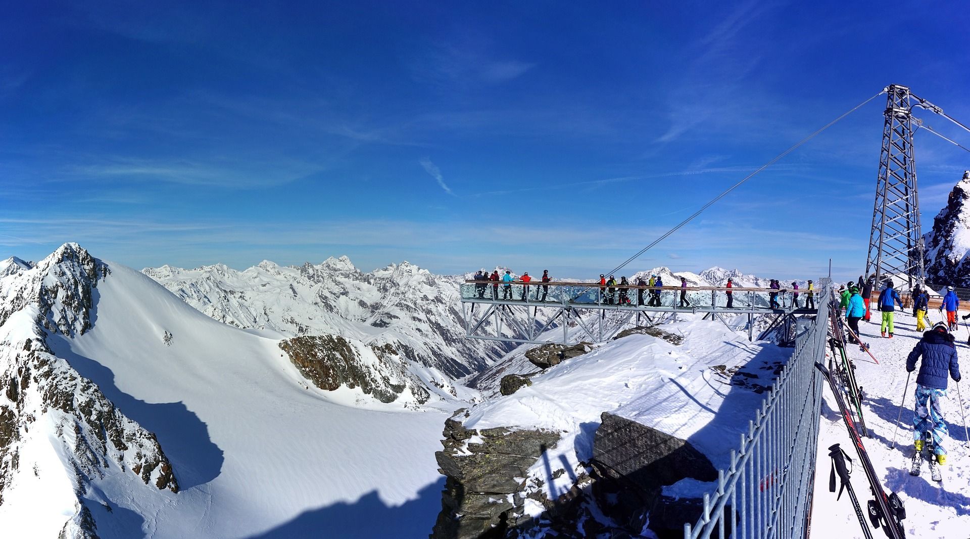 A WeRoad group trip on a viewing platform overlooking a vast, snow-covered mountain range under a clear blue sky.