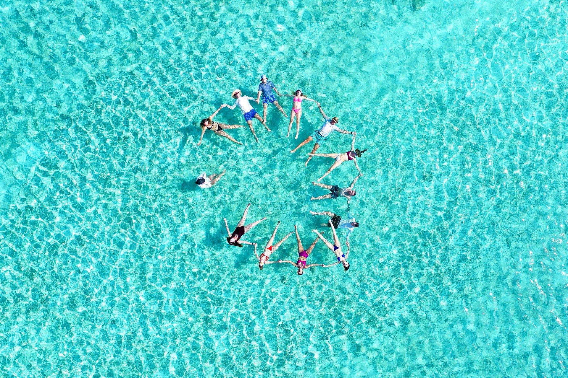 Un viaje en grupo de WeRoad tomados de las manos en círculo mientras flotan de espaldas en aguas claras de color turquesa.