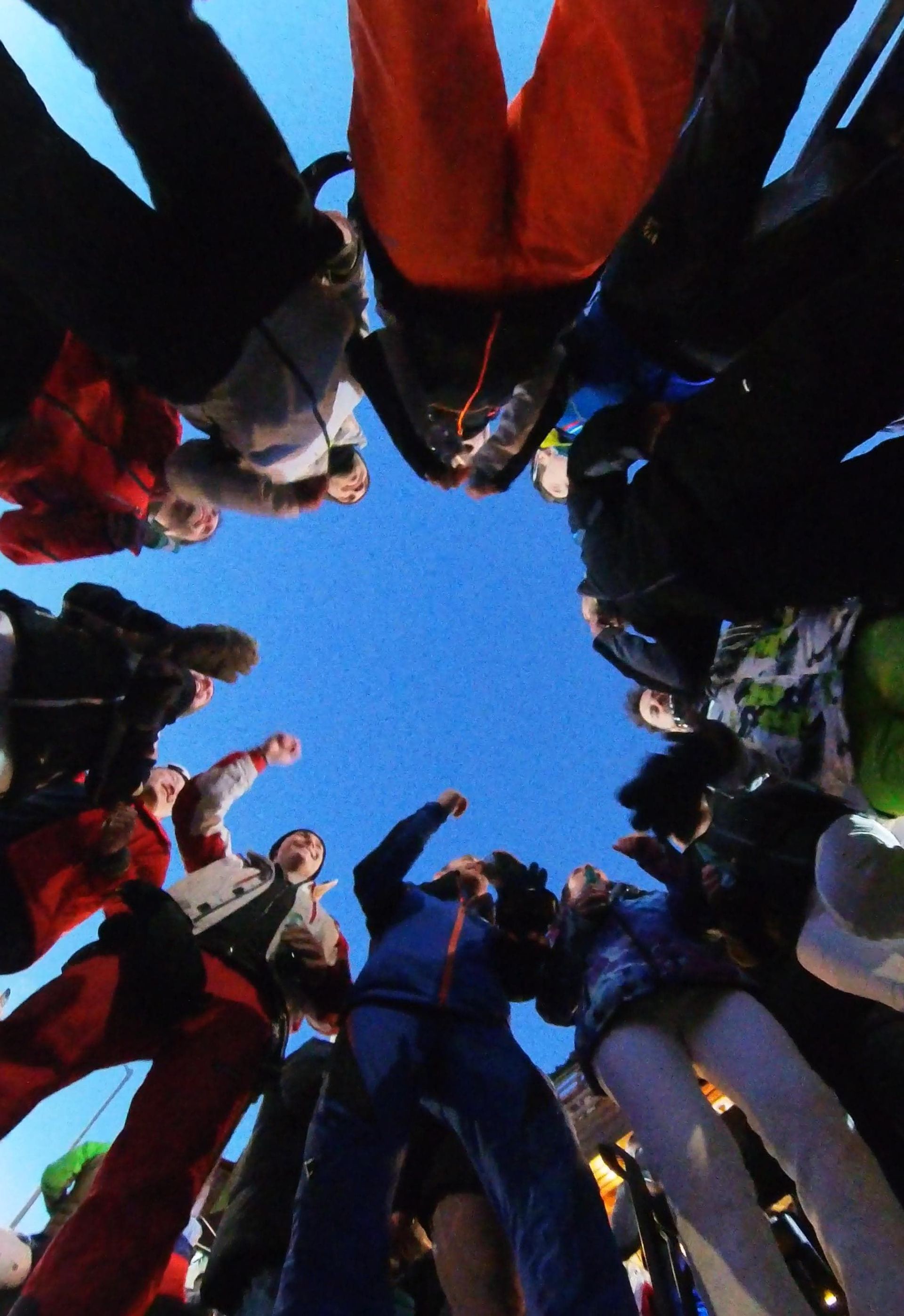 Una vista en ángulo bajo de un grupo de viaje de WeRoad reunido en círculo, mirando hacia abajo bajo un cielo azul claro.
