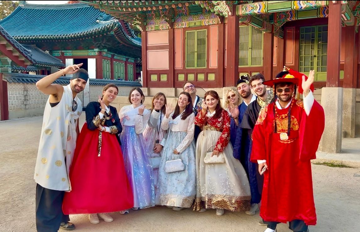 Un gruppo WeRoad sorride e posa per una foto in abiti tradizionali coreani davanti a un palazzo storico.