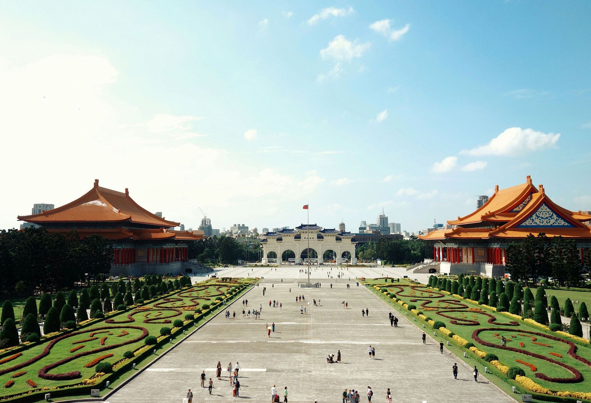 Una veduta dall'alto di una grande piazza con persone, fiancheggiata da tradizionali edifici asiatici con tetti arancioni e giardini curati.