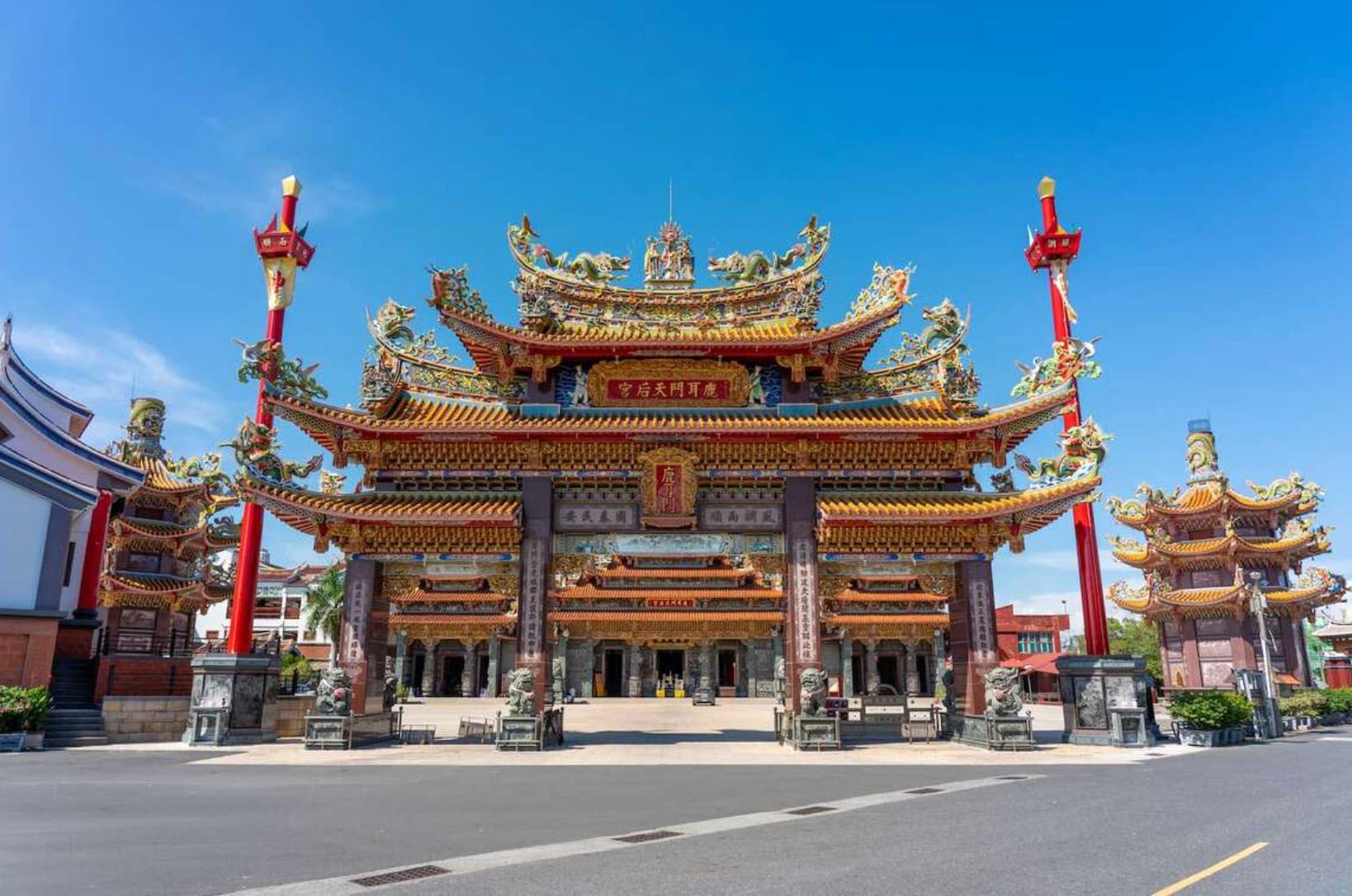 Un grande e ornato portale di un tempio dell'Asia orientale, con un tetto colorato e dettagliato, si erge al di là di una strada sotto un cielo azzurro e limpido.